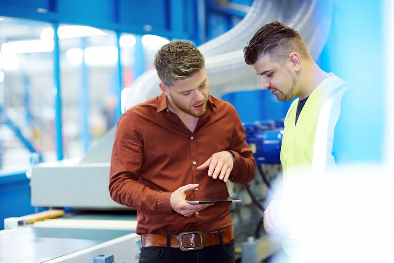 Two professionals on a manufacturing floor engage in a training session, one in a high-vis vest, demonstrating the empowerment of a skilled team through focused digital training, as highlighted in our latest blog post on team development in the industry
