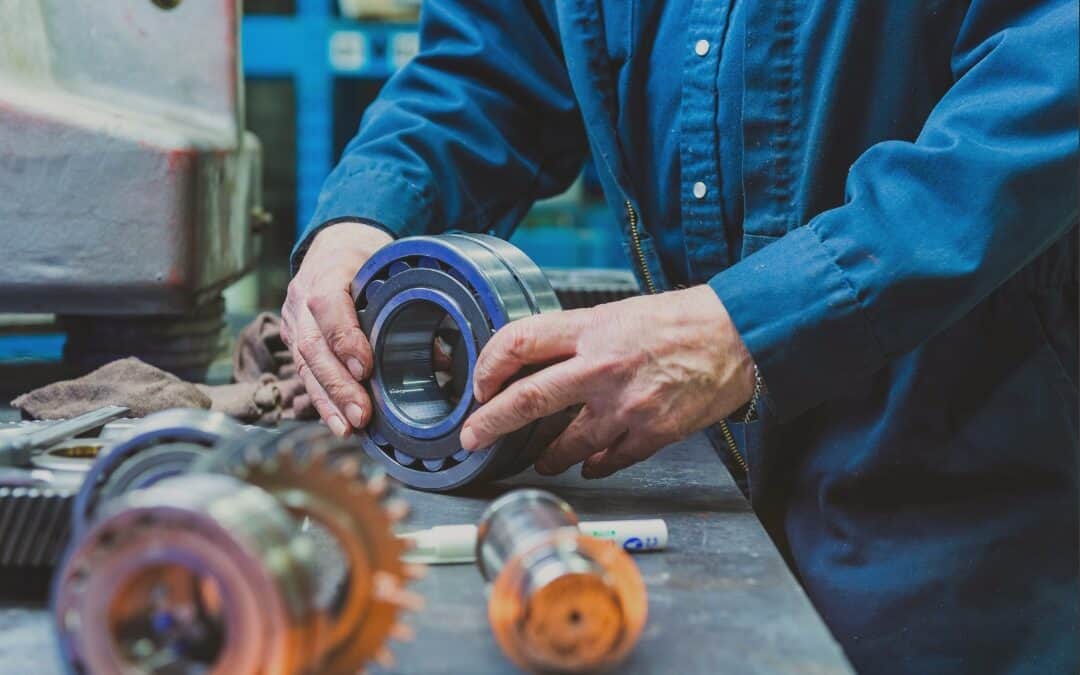 A meticulous engineer in a blue work shirt inspects a high-precision bearing component on a workshop bench, symbolizing the practice of improving manufacturing quality, which is the focal theme of the blog post titled 'Improving Manufacturing Quality: 5 Simple Steps for 2024
