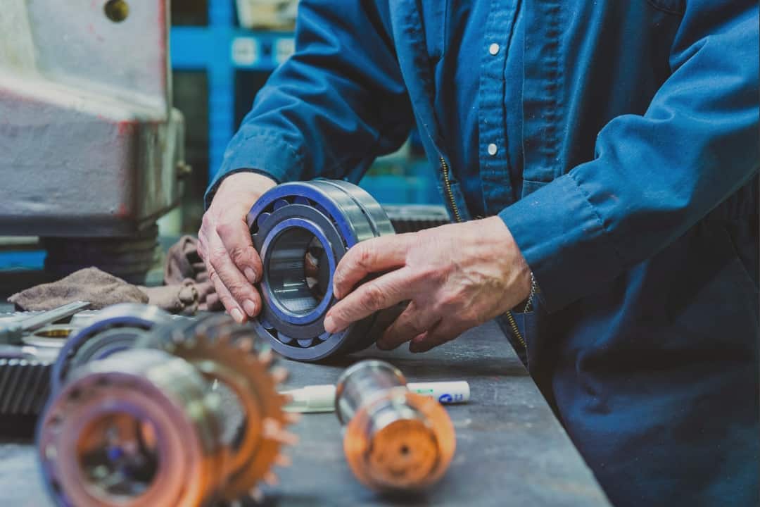 A meticulous engineer in a blue work shirt inspects a high-precision bearing component on a workshop bench, symbolizing the practice of improving manufacturing quality, which is the focal theme of the blog post titled 'Improving Manufacturing Quality: 5 Simple Steps for 2024